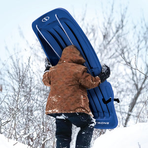 Kid carrying the Snow Joe 48-inch blue-colored kids snow sled up a hill.