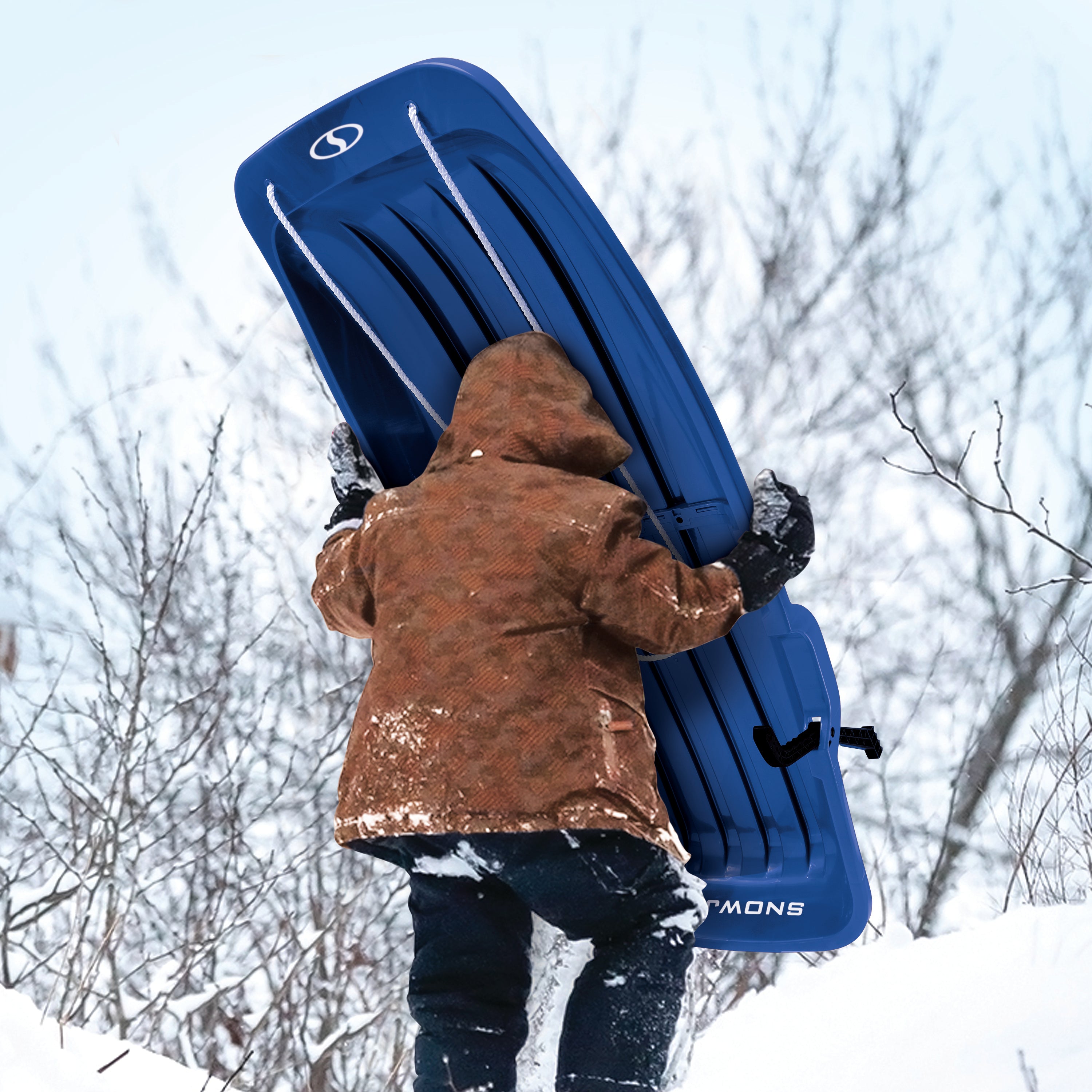Kid carrying the Snow Joe 48-inch blue-colored kids snow sled up a hill.
