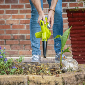 Person using the Sun Joe 24-volt cordless workshop blower with a 2.0-Ah lithium-ion battery attached to blow debris form a garden.