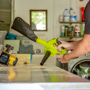 Person using the Sun Joe 24-volt cordless workshop blower with a 2.0-Ah lithium-ion battery and collection bag attached sucking up dust from a table.