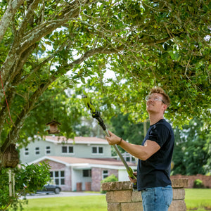 Man using the Sun Joe 24-volt Cordless Handheld and Long-Reach Pruner and Lopper to cut branches on a tree.