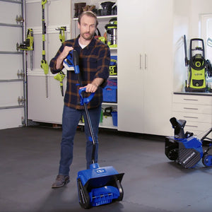 Man standing with the Snow Joe 24-volt cordless 13-inch snow shovel kit in a garage with other Snow Joe and Sun Joe tools on the wall.