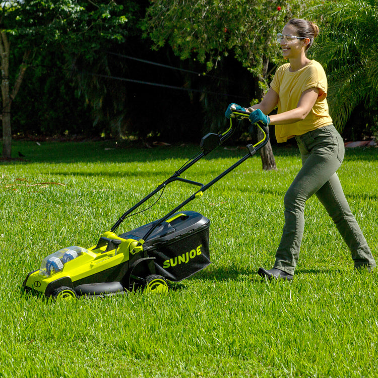 Woman using the Sun Joe 48-volt cordless 17-inch lawn mower kit to mow a lawn.