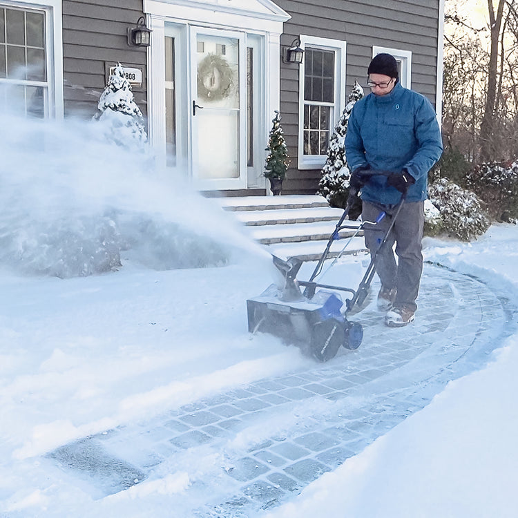 Man using the Snow Joe 48-volt cordless 18-inch snow blower kit to clear a front walkway of snow.