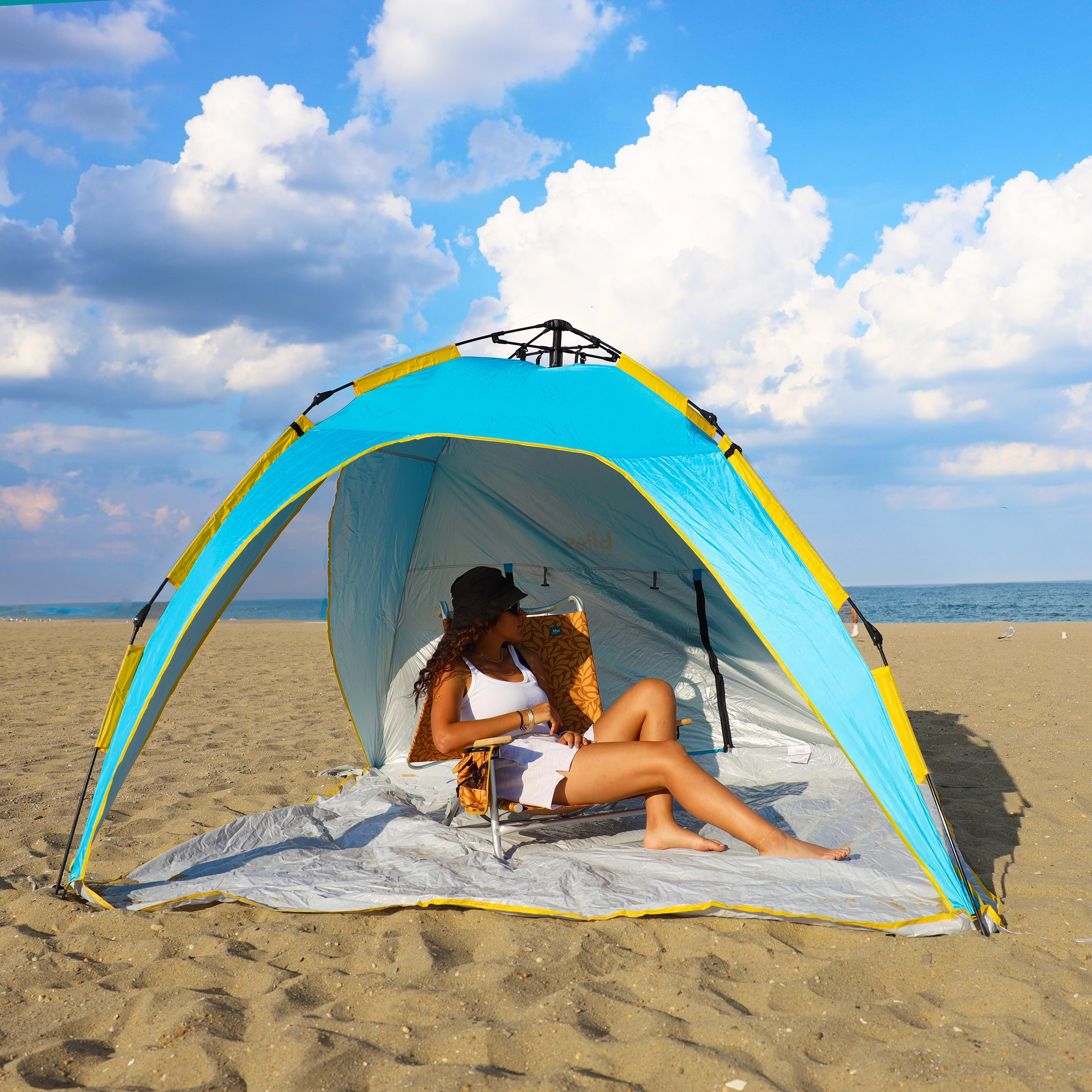 Woman relaxing in a chair on the beach while being shaded by the pop-up beach tent.