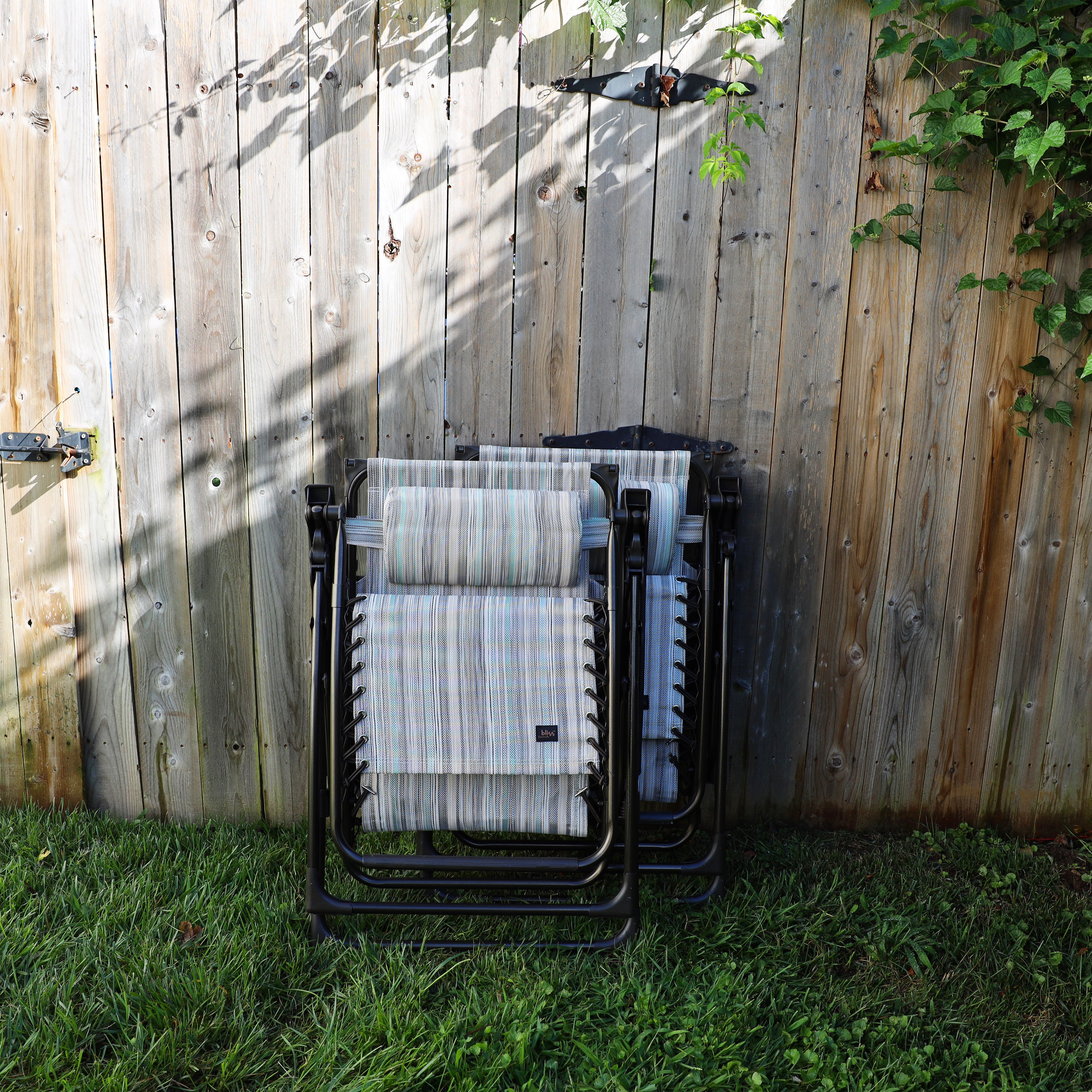 Set of 2 26-inch casual stripe gravity free chairs folded and leaning against a fence.