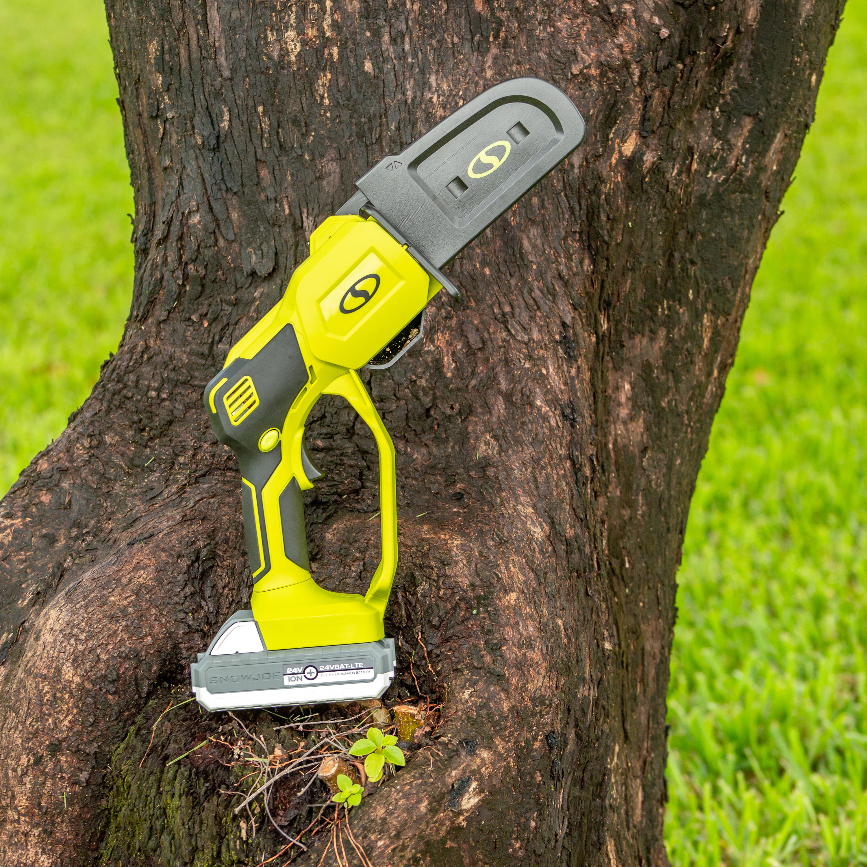 Sun Joe Cordless Handheld Chainsaw with its chain cover on, resting outside on a tree.