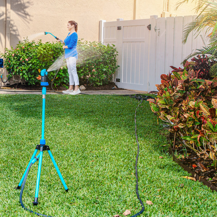 Aqua Joe Indestructible Turbo Drive 360 Degree Telescoping Tripod Lawn and Garden Sprinkler and Mister watering a lawn while a women waters a bush with an Aqua Joe hose and nozzle.