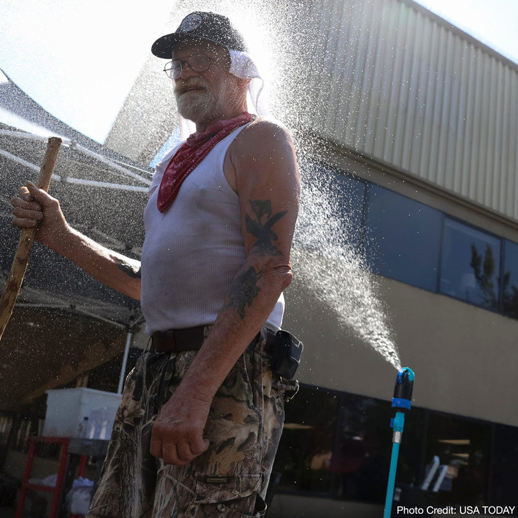 Man using the Aqua Joe 45-inch Indestructible Turbo Drive 360 Degree Telescoping Tripod Lawn and Garden Sprinkler and Mister to cool down on a hot day - from USA Today.