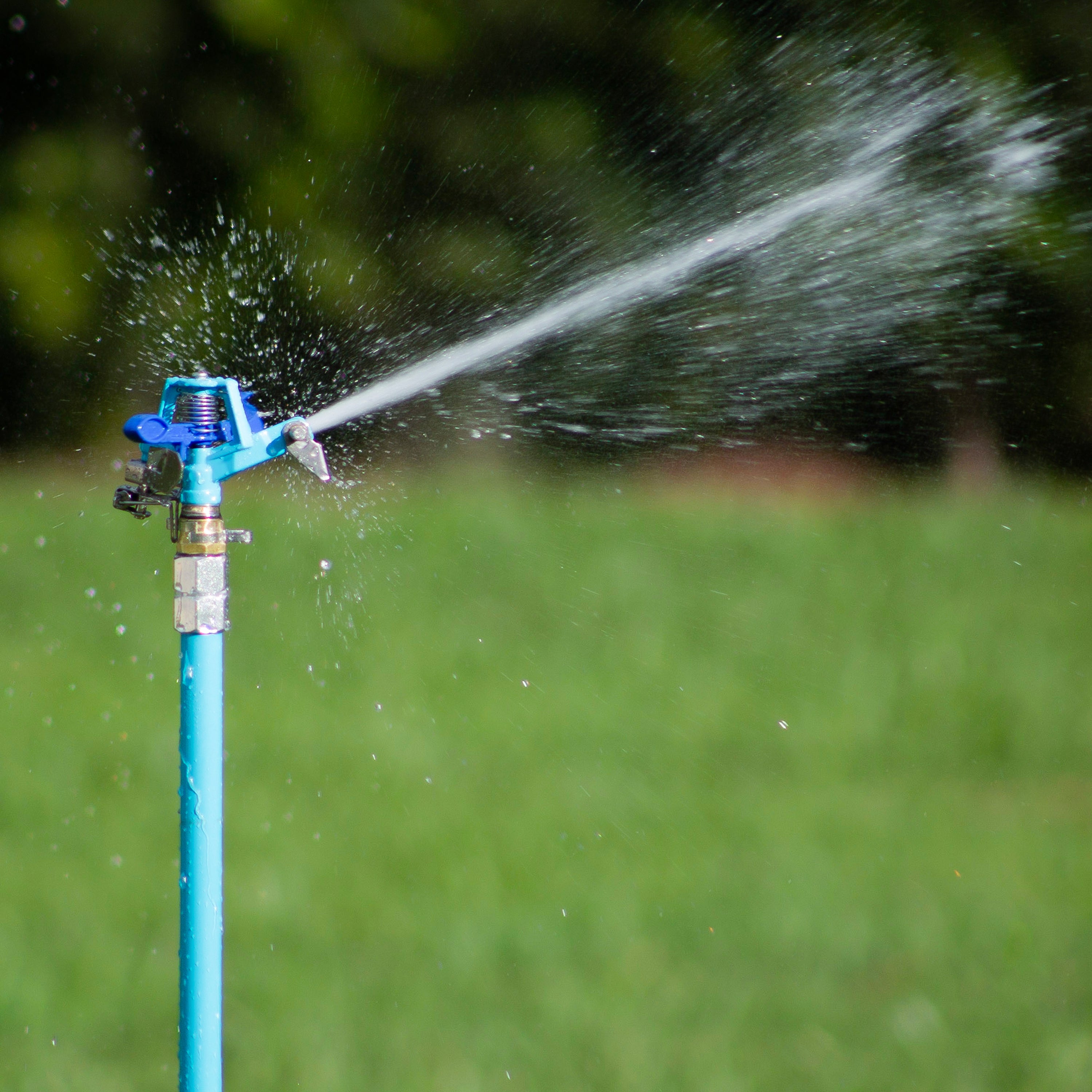 Close-up of the Aqua Joe 72-inch Indestructible Zinc Impulse 360-Degree Telescoping Tripod Sprinkler spraying water.