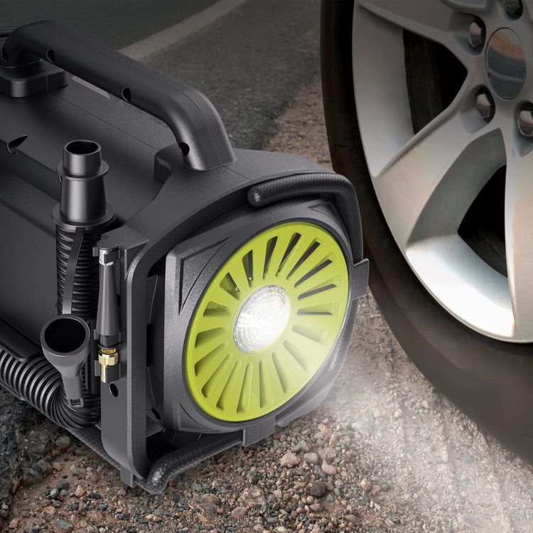 Sun Joe Hybrid 12-Volt/110-Volt AC High Volume Tire Inflator/Deflator next to a car tire with its headlight turned on.