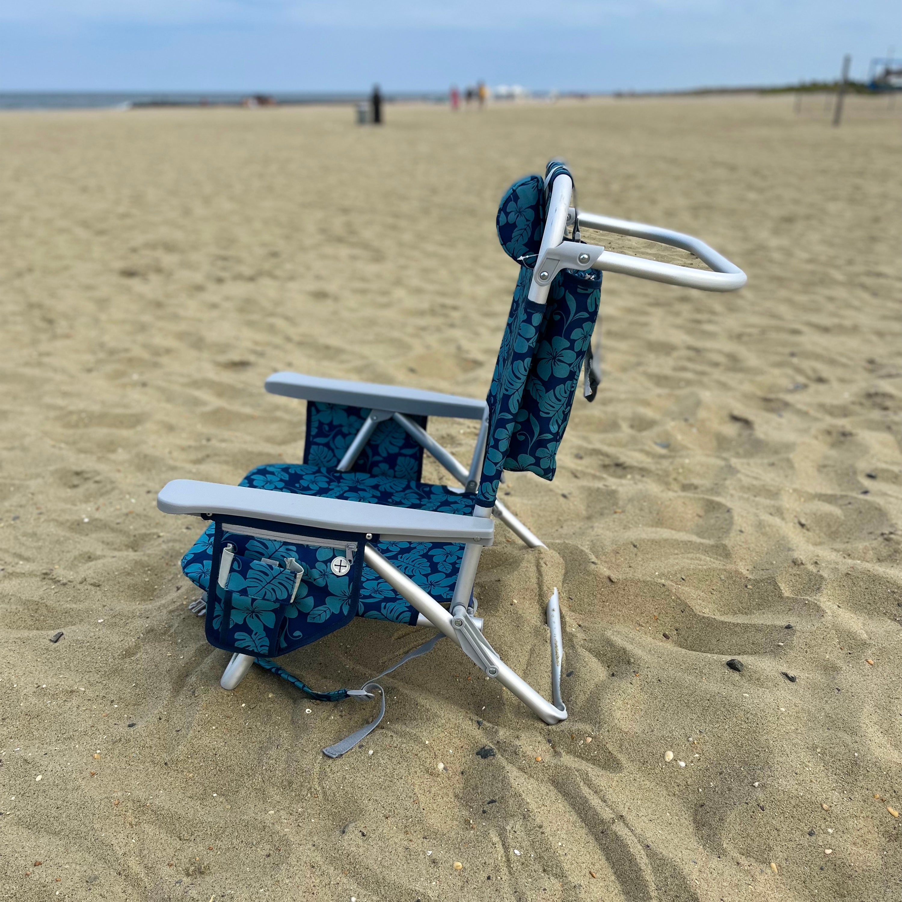 Side view of the blue flower backpack beach chair on the sand.