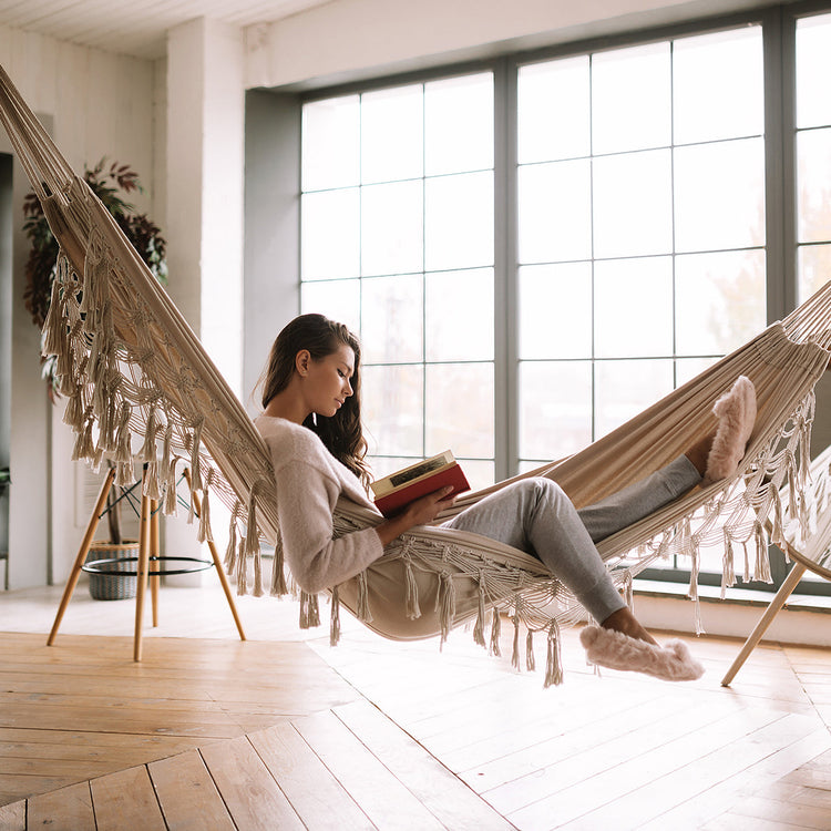 Woman reading a book while in the Bliss Hammocks 40" Wide Hammock in a Bag with Fringe hung up indoors.