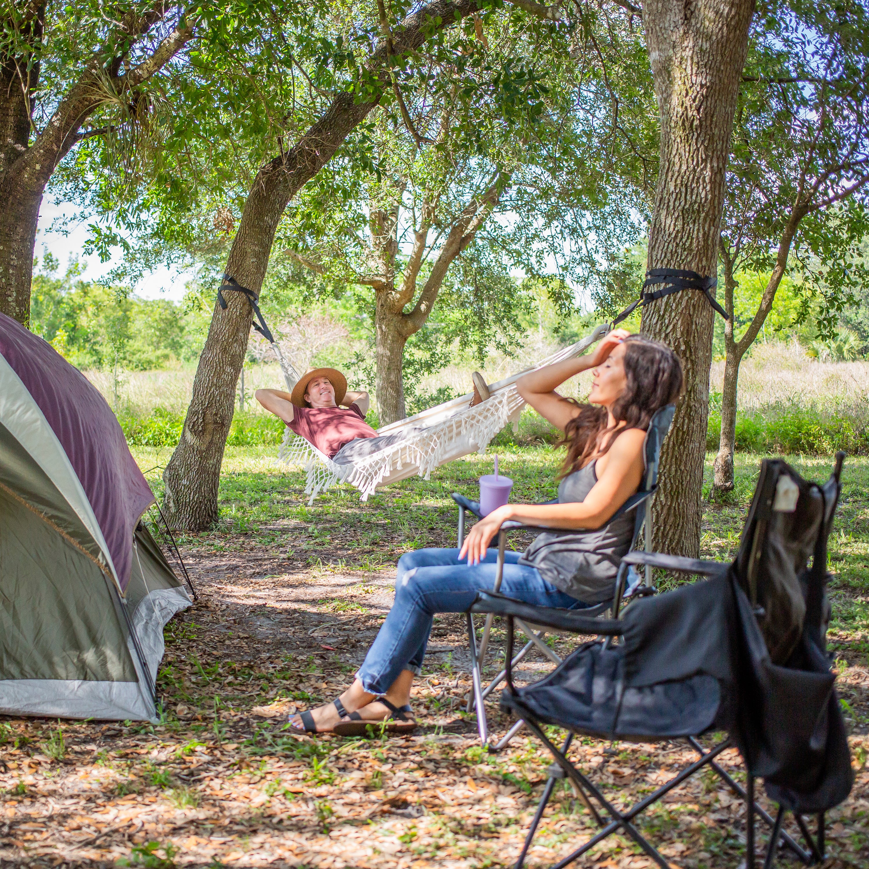 Woman relaxing in the Bliss Hammocks 40" Wide Hammock in a Bag with Fringe hung between two trees in a camp site.