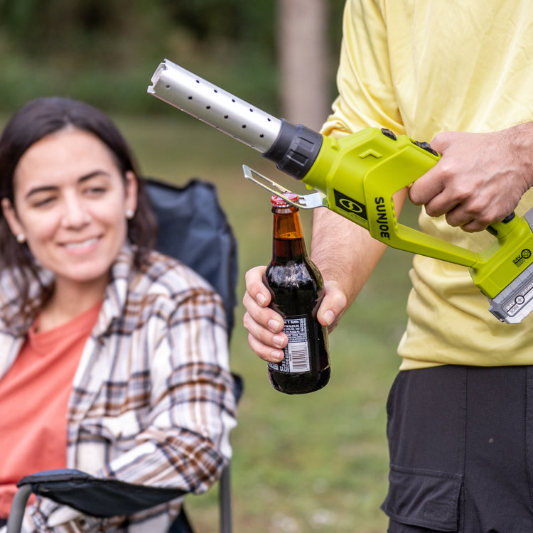 Person using the bottle opener on the Sun Joe 24-Volt cordless electric fire starter and barbeque lighter to take the cap off a bottle.