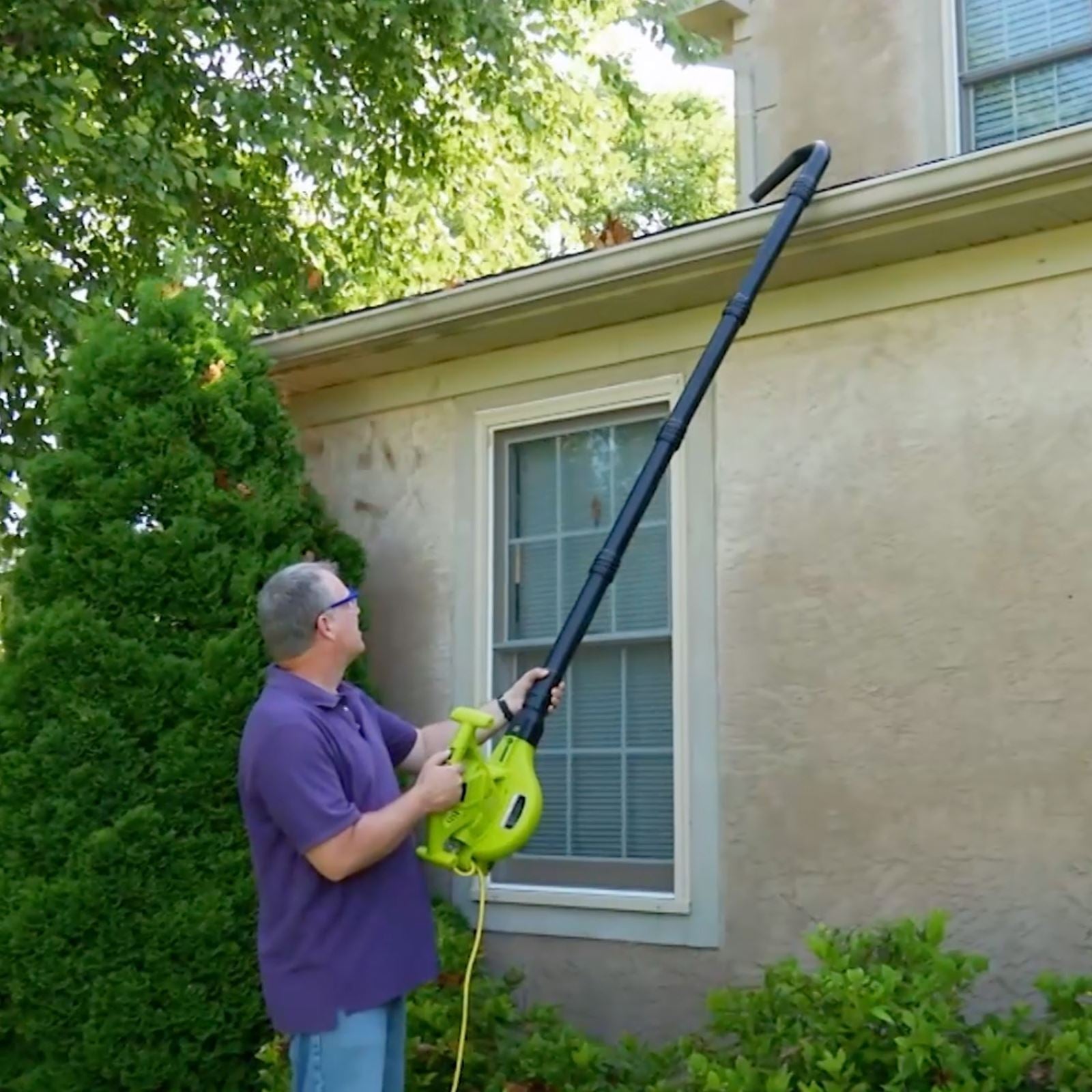 Person using the Sun Joe 14-amp high-performance 4-in-1 Electric Leaf Blower with the gutter attachment to blow leaves out of a gutter.