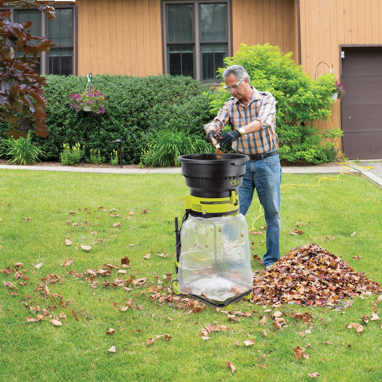 Man putting leaves into the Sun Joe 15-amp Bladeless Electric Leaf Mulcher and Shredder in a front lawn.