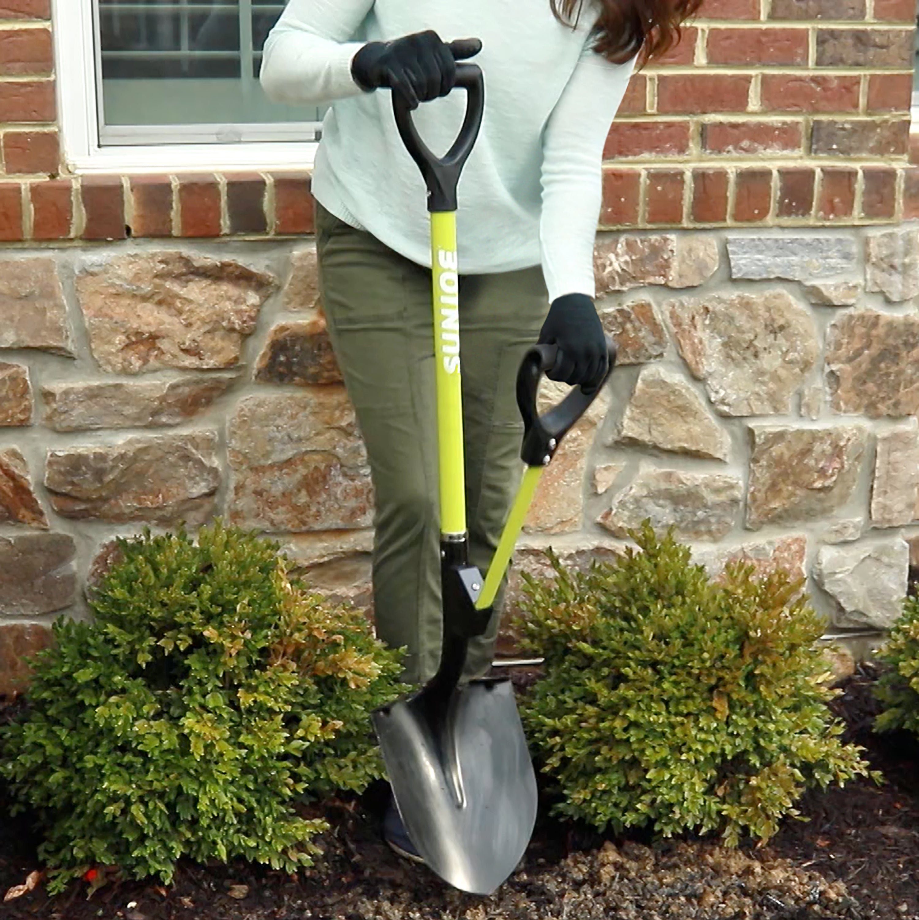 Sun Joe 9-inch Green Shovelution Strain-Reducing Utility Round-Point Digging Garden Shovel being used to dig a hole in a small garden.