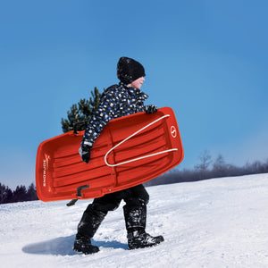 Kid carrying the Snow Joe 34-inch red-colored kids snow sled.