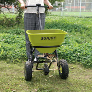 Sun Joe Multi-Purpose Walk-Behind Spreader being used to spread fertilizer on a lawn,