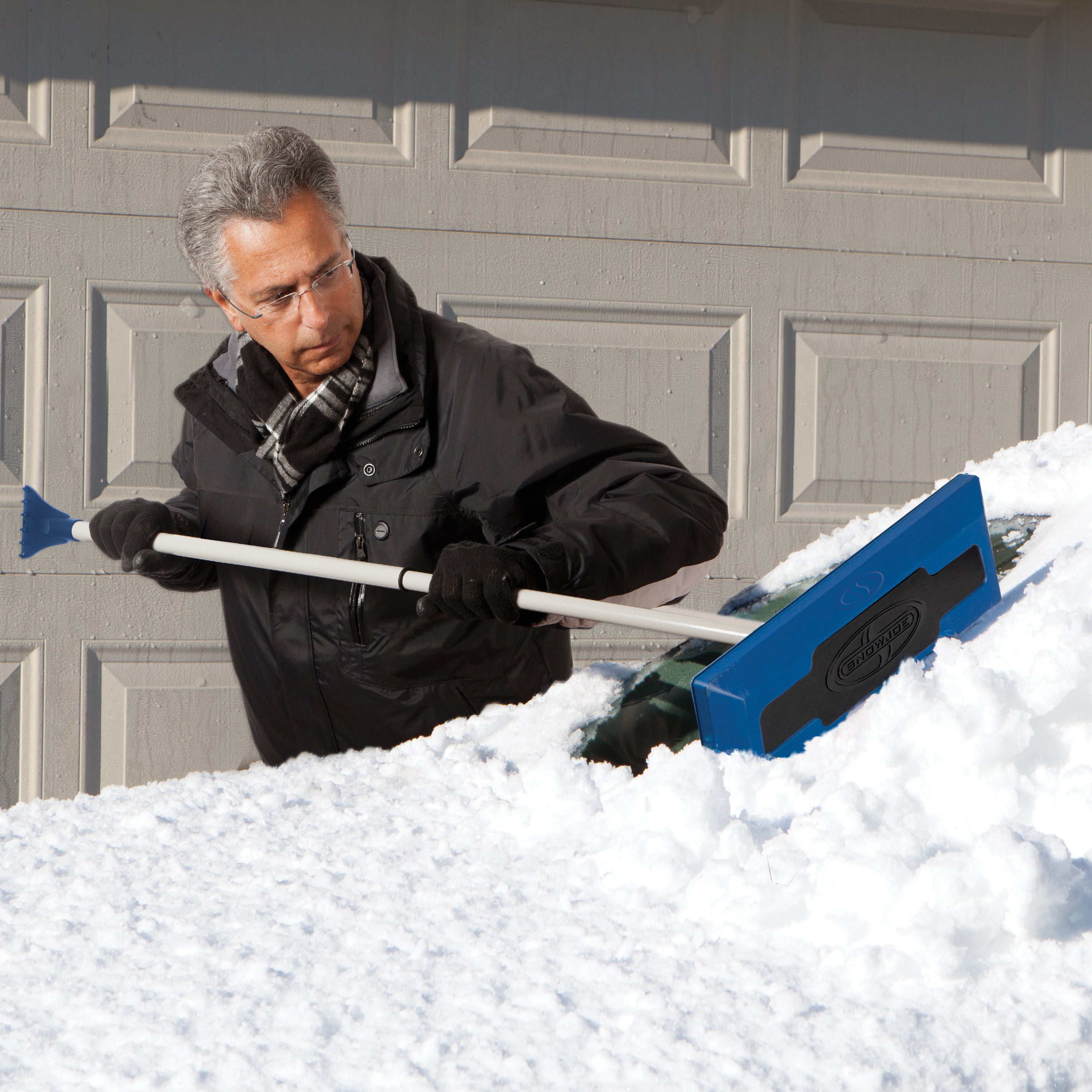 Snow Joe Snow Broom and ice scraper being used to push snow off a car windshield.