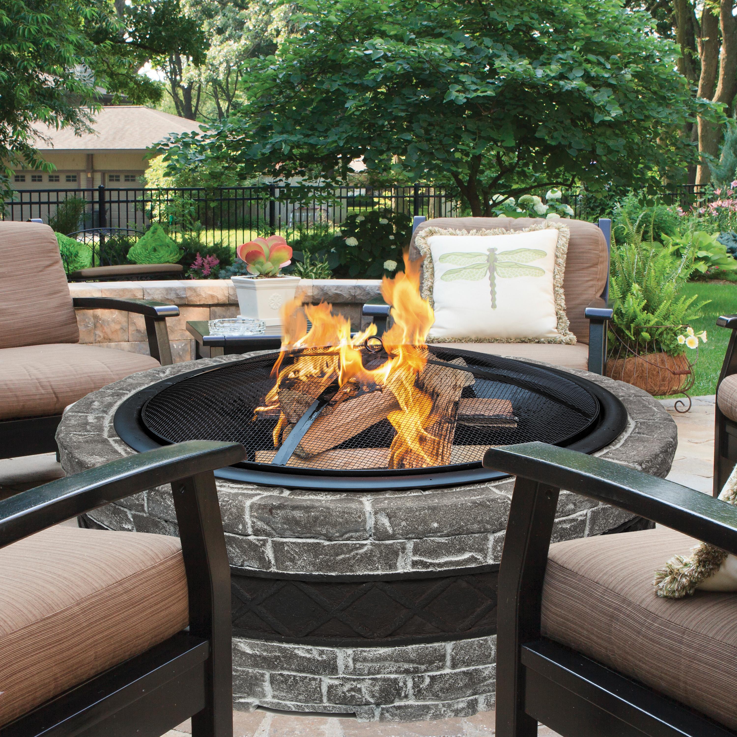 Fire going in the Sun Joe 35-Inch Charcoal stone Cast Stone Base, Wood Burning Fire Pit with patio chairs around it.