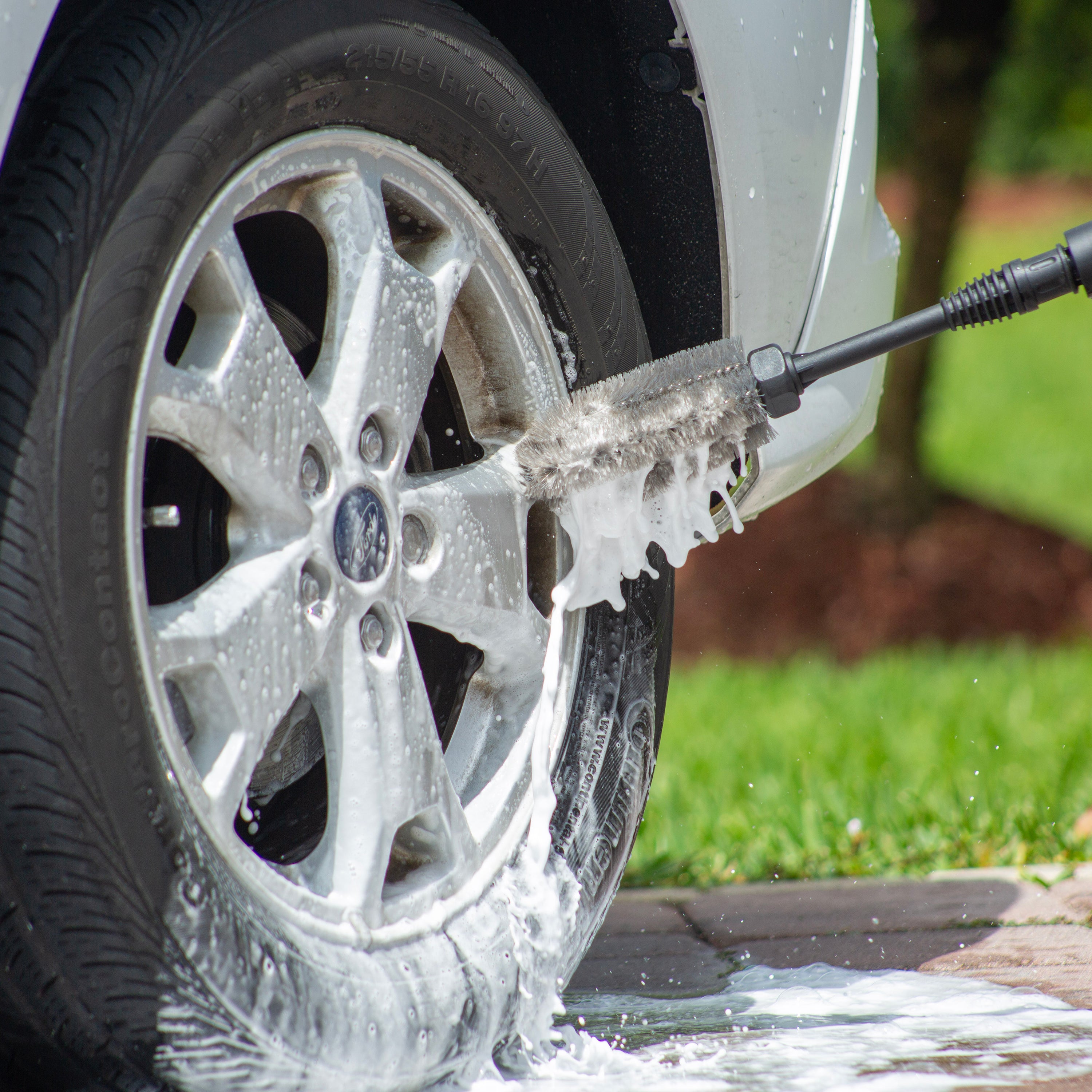 Sun Joe pressure washer detergent being used with the wheel and rim brush to clean a car tire.